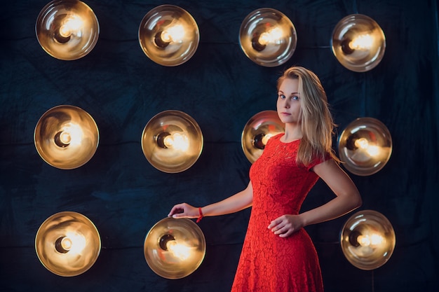 Holidays and fashion concept - beautiful sexy woman in red dress over lights background