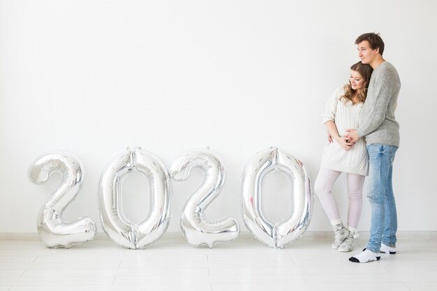 Holidays, festive and party concept - Happy loving couple near silver 2020 balloons. New Year celebration