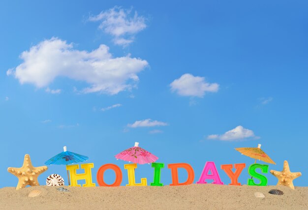 Holidays letters on a beach sand against the blue sky