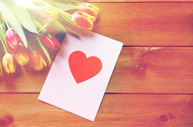 休日、愛、バレンタインデーのコンセプト - チューリップの花と木製のテーブルに心でグリーティング カードのクローズ アップ
