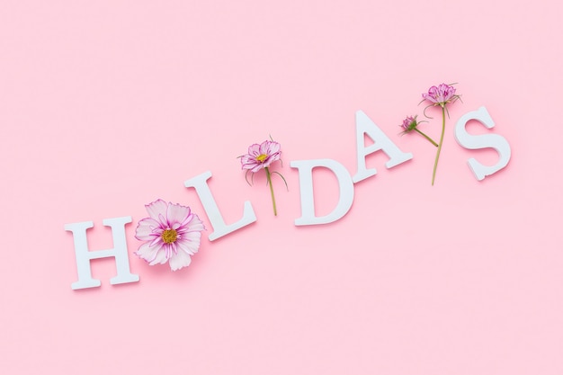 Holidays. Motivational quote from white letters and beauty natural flowers on pink background. Creative concept inspirational quote.