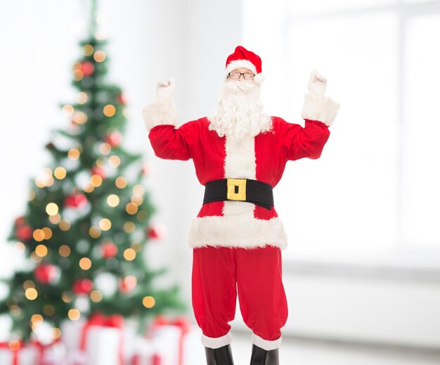 holidays and people concept - man in costume of santa claus having fun over living room and christmas tree background