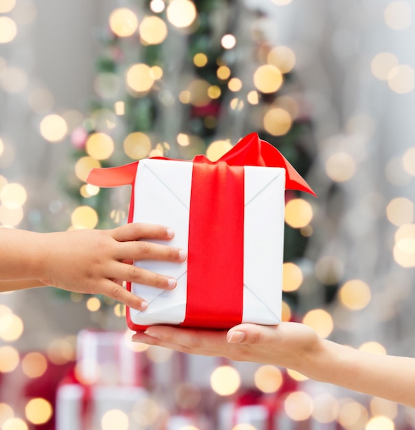 Concetto di vacanze, presente, infanzia e felicità - primo piano delle mani del bambino e della madre con confezione regalo su sfondo di luci dell'albero di natale