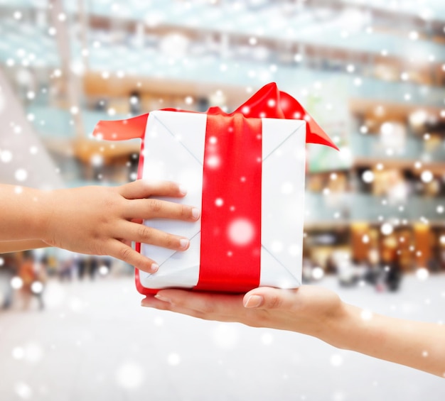 holidays, present, christmas, childhood and happiness concept - close up of child and mother hands with gift box over shopping center background