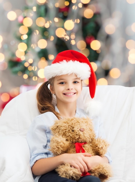 holidays, presents, childhood and people concept - smiling little girl with teddy bear toy over living room and christmas tree background