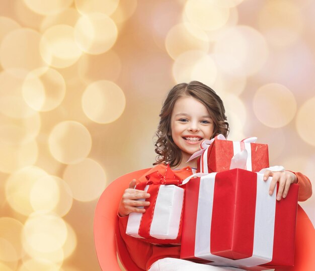 holidays, presents, christmas, childhood and people concept - smiling little girl with gift boxes over beige lights background