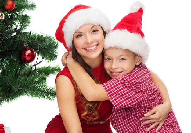 праздники, подарки, рождество, рождественская концепция - счастливая мать и ребенок мальчик в шапках санта-помощника