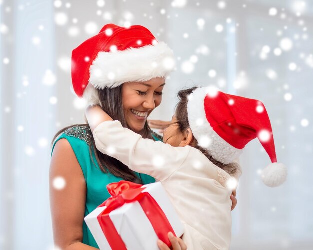 holidays, presents, christmas, x-mas concept - happy mother and child girl in santa helper hats with gift box