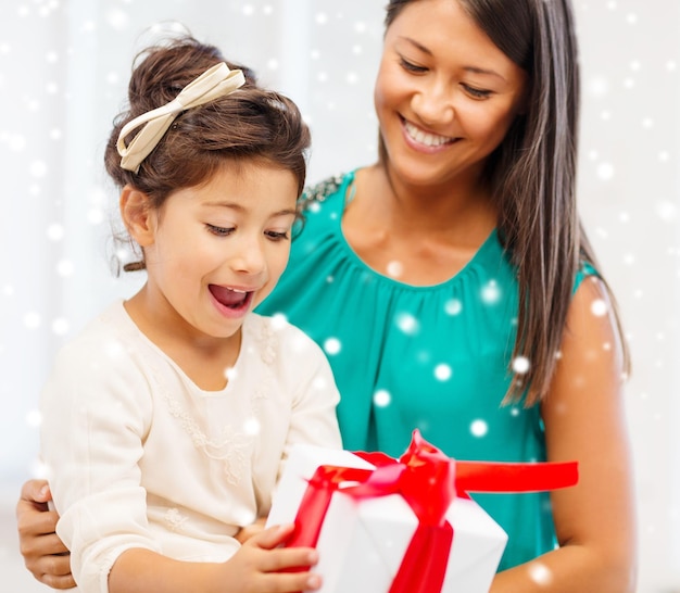 holidays, presents, christmas, x-mas concept - happy mother and child girl with gift box over snowy background