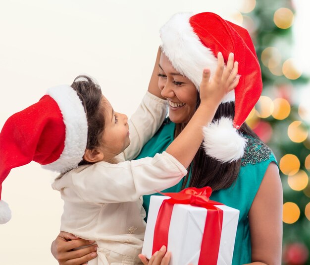 휴일, 선물, 크리스마스, 크리스마스 개념 - 선물 상자가 있는 산타 도우미 모자를 쓴 행복한 엄마와 아이 소녀