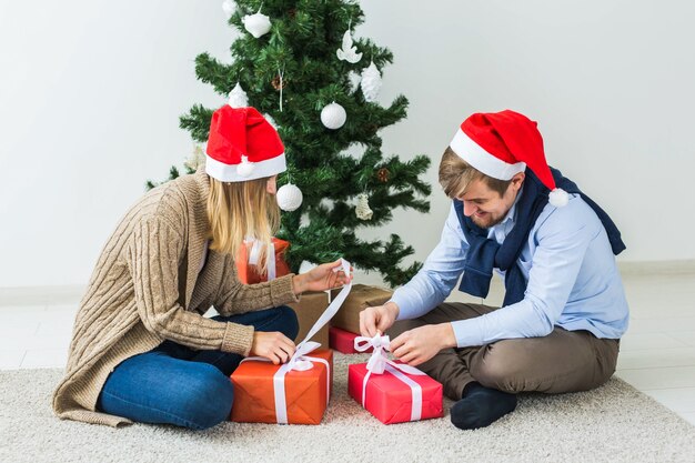 休日、関係、お祭りのコンセプト-クリスマスツリーで一緒にプレゼントを開くカップル。