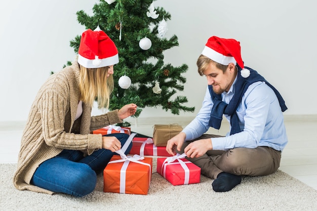 休日、関係、お祭りのコンセプト-クリスマスツリーで一緒にプレゼントを開くカップル