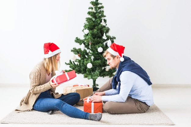 Holidays, relationship and festive concept - Couple opening present together by Christmas tree