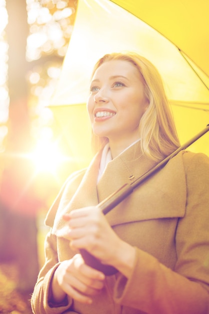 休日、季節、旅行、観光、幸せな人々の概念-秋の公園で黄色い傘を持つ笑顔の女性