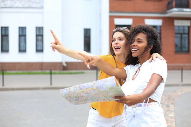 Holidays and tourism concept - beautiful girls looking for direction in the city.