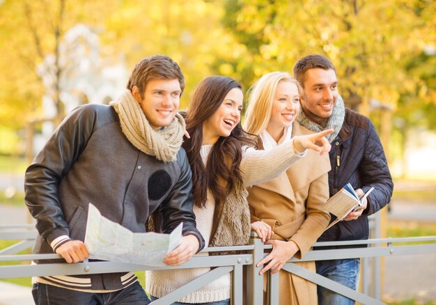 holidays and tourism concept - group of friends or couples with tourist map in autumn park