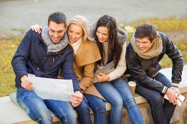 holidays and tourism concept - group of friends or couples with tourist map in autumn park