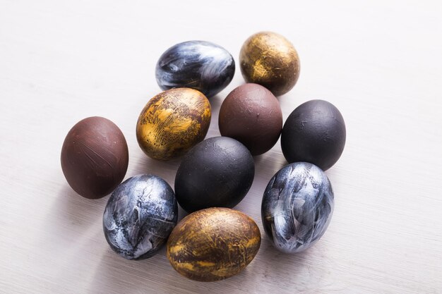 Праздники, традиции и концепция Пасхи - темные стильные пасхальные яйца на белом деревянном фоне.