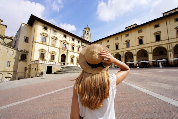 Праздники в Тоскане Вид сзади на путешественницу, держащую шляпу на площади Пьяцца Гранде в старом городе Ареццо Тоскана Италия