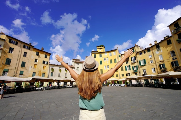 トスカーナの休日イタリアのルッカの歴史的な丸い広場アンフィテアトロ広場で腕を上げる若い観光客の女性