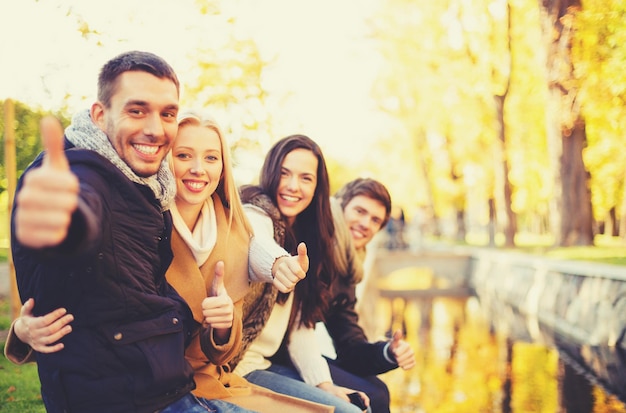 Vacanze, vacanze, concetto di persone felici - gruppo di amici o coppie che si divertono e mostrano i pollici in su nel parco autunnale