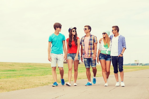 концепция праздников, каникул, любви и дружбы - группа улыбающихся подростков, гуляющих на свежем воздухе