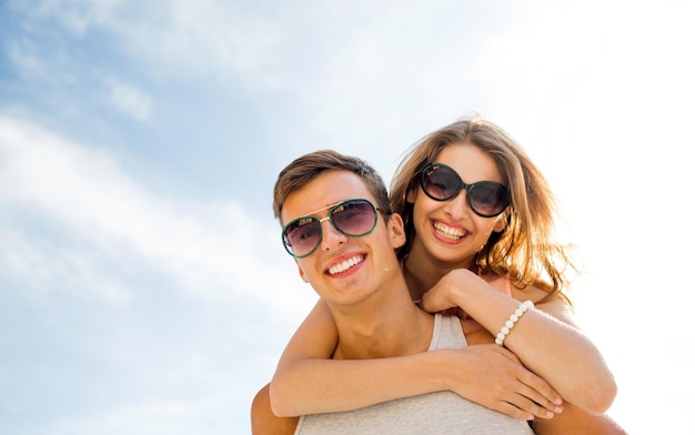 holidays, vacation, love and friendship concept - smiling couple having fun over sky background