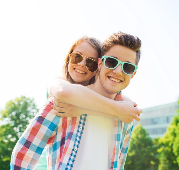 holidays, vacation, love and friendship concept - smiling teen couple in sunglasses having fun in summer park