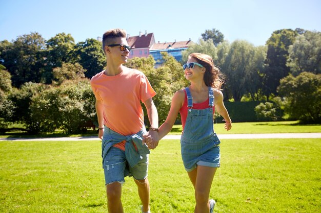 Foto concetto di vacanze, vacanze, amore e persone - coppie adolescenti sorridenti felici che camminano e si guardano l'un l'altro nel parco estivo