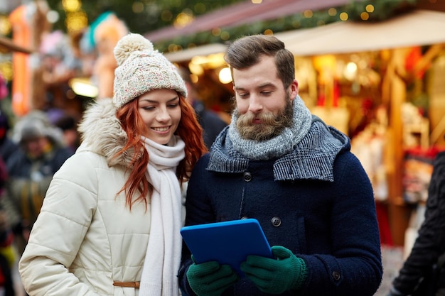 holidays, winter, christmas, technology and people concept - happy couple of tourists in warm clothes with tablet pc computer walking in old town