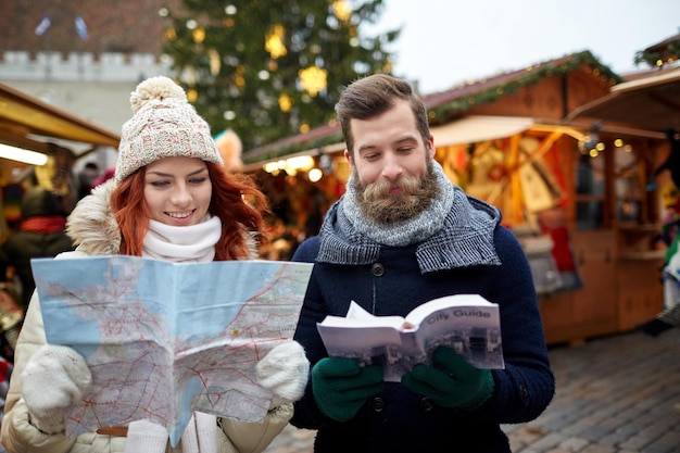 휴일, 겨울, 크리스마스, 관광 및 사람 개념 - 구시가지의 지도 및 도시 가이드가 있는 따뜻한 옷을 입은 행복한 커플