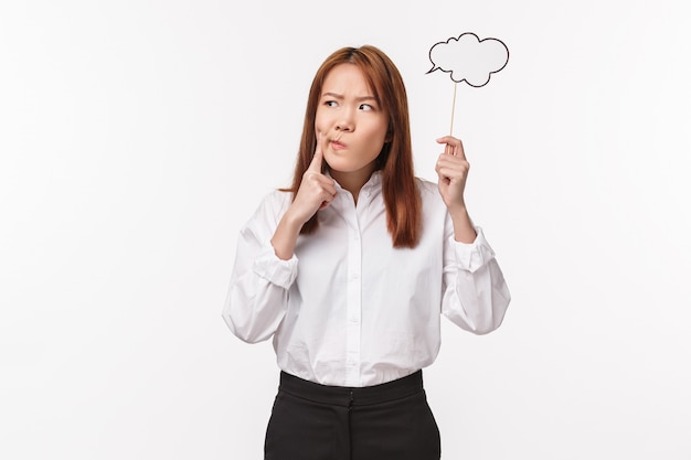 Holidays, women and lifestyle concept. Portrait of thouhgtful serious-looking hesitant asian woman holding thinking cloud on stick, grimacing and touch lip pondering, look away, 