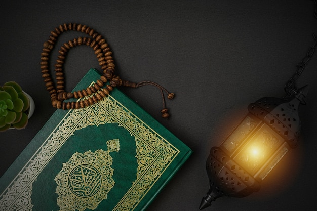 Holy Al Quran with written arabic calligraphy meaning of Al Quran and rosary beads on black