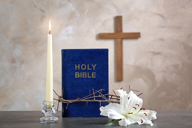 Holy Bible crown of thorns lily candle and cross on beige background