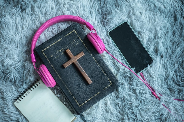 Holy bible with headphones smartphone and wooden cross