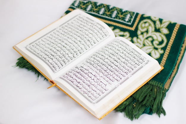 The holy book al quran and prayer rug isolated on white background