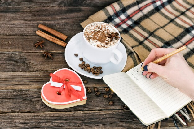 Holyday ochtend planning. Kopje cappuccino, vrouwelijke hand met een potlood en Kladblok op een bruine houten tafel