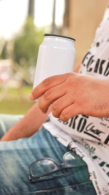 Photo hombre sosteniendo lata blanca con la mano. tomando soda en el parque. sentado en el parque