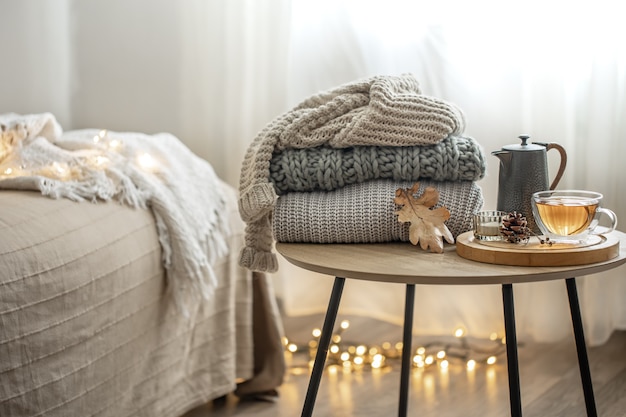 Home autumn composition with tea and knitted sweaters in the interior of the room, on a blurred background.