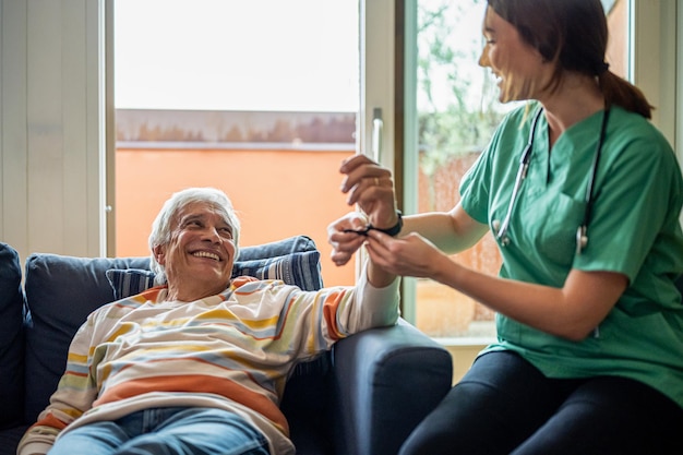 Foto badante domiciliare che esamina l'uomo anziano controllando i segni vitali da un orologio intelligente per l'infermiera di diagnosi sanitaria che aiuta l'occupazione della dottoressa anziana al coperto