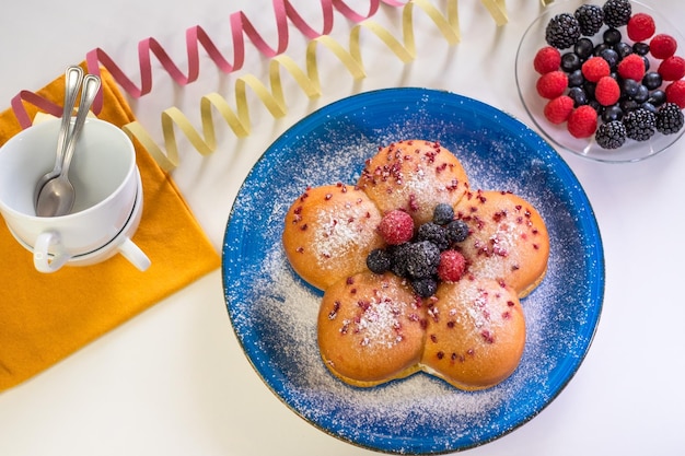 Concetto di cucina casalinga pane al latte dolce fresco biologico fatto in casa ripieno di crema e decorato con frutti di bosco su piatto blu