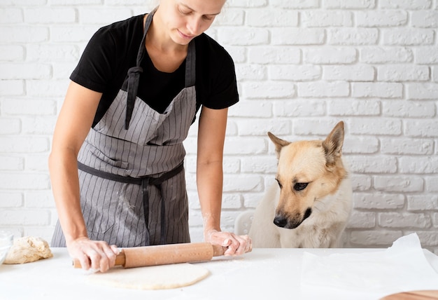 家庭料理。そばに座っている犬と一緒に家で生地をこねる女性