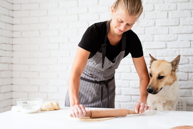 家庭料理。そばに座っている犬と一緒に家で生地をこねる女性