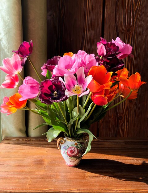 家の装飾と花束の配置の芸術窓の近くの木製のテーブルの内部に庭のカラフルなチューリップが付いた春のロマンチックな花束