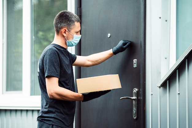 Фото Доставка на дом коробка покупок человек в перчатках и защитной маске с доставкой посылок к двери