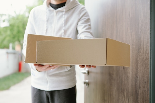 Home delivery shopping box man wearing gloves and protective mask delivering packages at door.