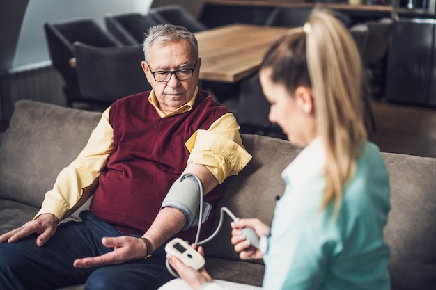 Home doctor is measuring blood pressure of old man at his home Professional health support