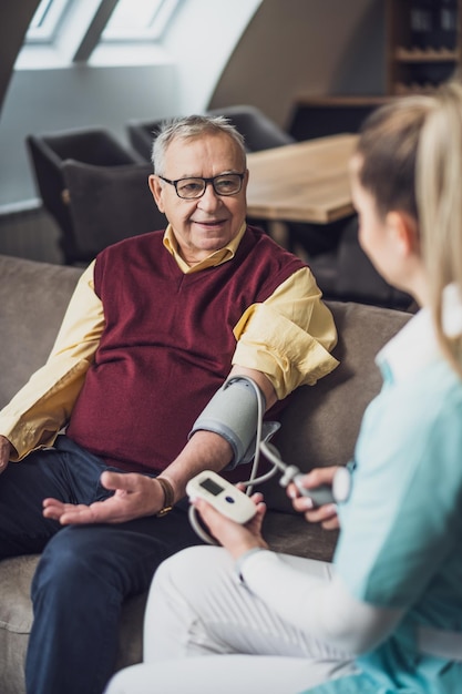 Home doctor is measuring blood pressure of old man at his home Professional health support