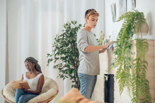 Foto a casa. ragazza bionda che pulisce la stanza, la sua ragazza seduta sulla sedia