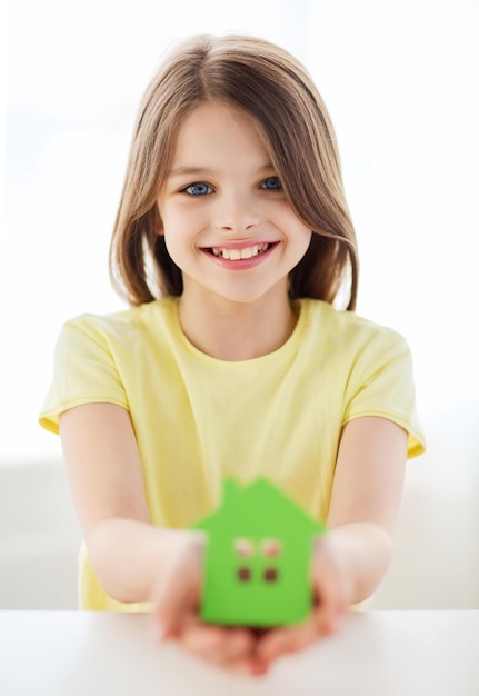 концепция дома и семьи - маленькая девочка держит дом из зеленой бумаги